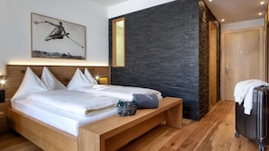 A modern hotel room with a wooden bed, a bench, a suitcase, and a stone accent wall. - Wadhotel National (Arosa)