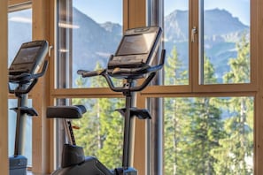 A gym with stationary bikes and a view of a mountainous landscape through large windows. - Wadhotel National (Arosa)