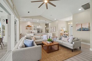 A spacious living room with a large sectional sofa, a coffee table, and a ceiling fan. - Palms on 45th | Gulf Access, Heated Pool & Spa (Cape Coral)