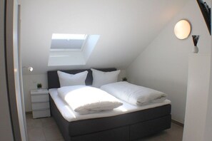 A bedroom with a skylight, a bed with white linens, a bedside table with a lamp, and a small plant. - Sonnengarten 21 in Kellenhusen (Kellenhusen)