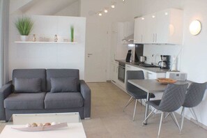 A modern living room with a grey sofa, a dining table with chairs, and a kitchen area with white cabinets and appliances. - Sonnengarten 21 in Kellenhusen (Kellenhusen)