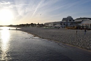 A beach with a building in the background, a clear sky, and a few people walking. - Dinius Schützenstraße (Grömitz)