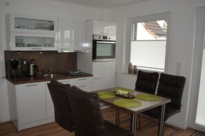 A compact kitchen with white cabinets, a built-in oven, and a dining area with a table and chairs. - Dinius Schützenstraße (Grömitz)