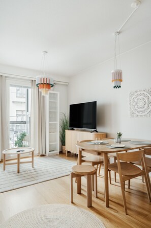 Ein modernes Wohnzimmer mit Essbereich, einem Flachbildfernseher und einem großen Fenster.