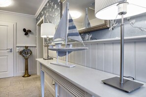 Ein Badezimmer mit weißem Waschtisch, einem Handtuchhalter im Schiffsdesign, einem wandmontierten Spiegel und einer klassischen Wanduhr.