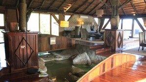 A rustic interior with a stone wall, wooden furniture, and a small water feature. - Serena Mivumo River Lodge (Selous Game Reserve)