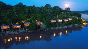 A series of overwater bungalows with thatched roofs, surrounded by lush greenery and reflecting on calm water. - Serena Mivumo River Lodge (Selous Game Reserve)