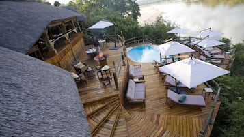 Een houten terras met een zwembad, ligbedden en parasols met uitzicht op een wateroppervlak.