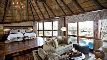 Een kamer met rieten dak, een bank, een bed en uitzicht op de omgeving.