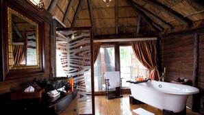 A wooden cabin bathroom with a bathtub, wooden vanity, and a large mirror. - Serena Mivumo River Lodge (Selous Game Reserve)