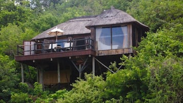Een houten boomhut met een balkon, omgeven door weelderige begroeiing.