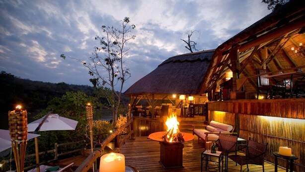 An outdoor deck with a fire pit, seating, and umbrellas. - Serena Mivumo River Lodge (Selous Game Reserve)