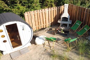 Ein Garten mit Holzzaun, Grill aus Stein und zwei grünen Lounge-Sesseln mit Heineken-Logo.