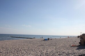 Ein Strand mit einem Steg, der sich ins Wasser erstreckt, einem sandigen Ufer und einigen verstreuten Personen.