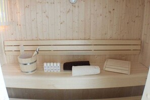 Eine Sauna mit einer Holzbank, einem Eimer, Handtüchern und Ölflaschen.