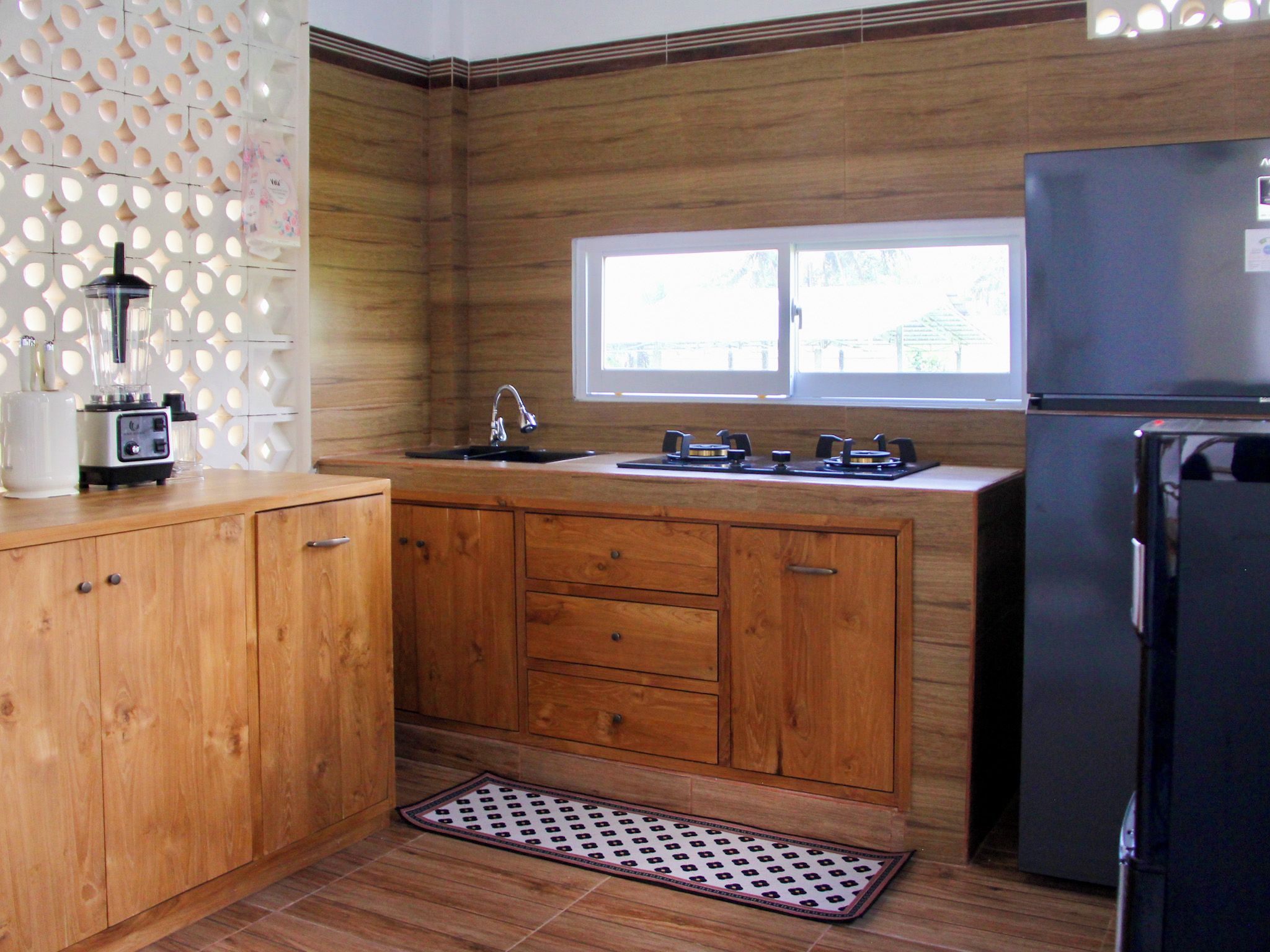 A kitchen with wooden cabinets, a black refrigerator, a window, and a sink.