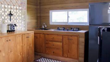 A kitchen with wooden cabinets, a black refrigerator, a window, and a sink.