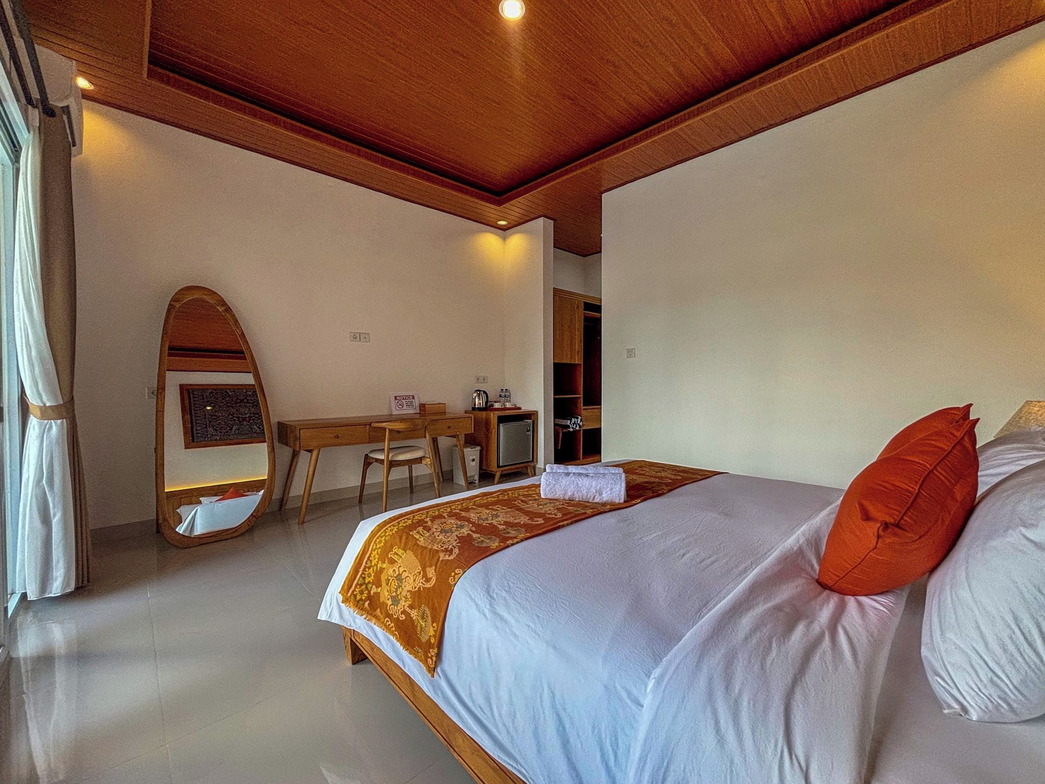 A bedroom with a bed, a desk, a mirror, and a wardrobe.