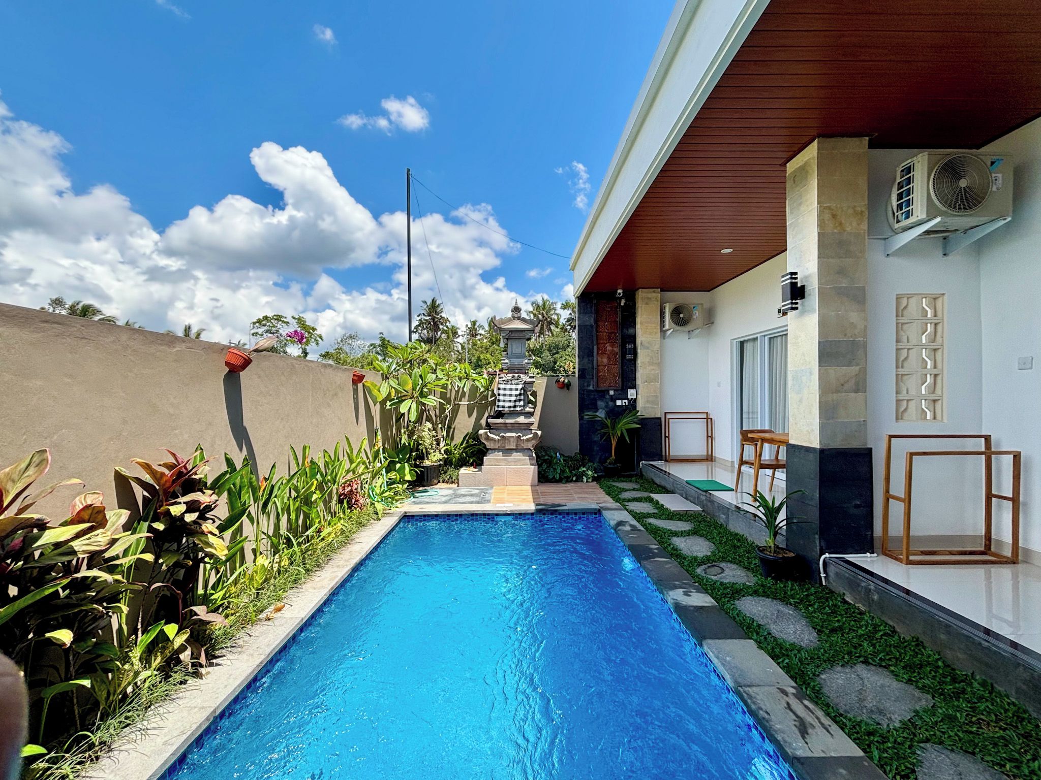 A swimming pool with a stone-lined edge, a covered patio area with seating, and a view of a temple in the distance.