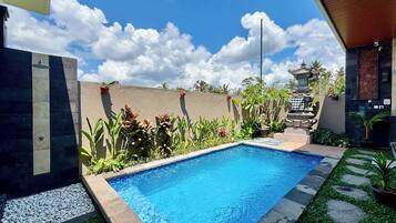 A swimming pool with a tiled edge, surrounded by a low stone wall, and a variety of plants.