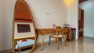 Habitación de hotel con escritorio de madera, una silla, refrigerador pequeño, mesita de noche con cama y un espejo grande.