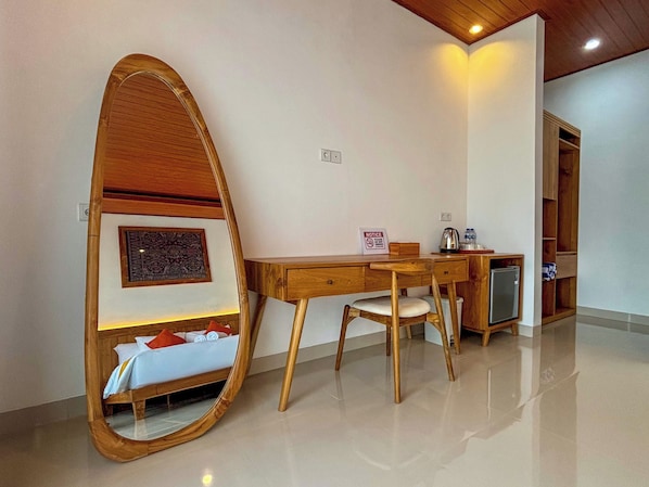 Une chambre d’hôtel avec un bureau en bois, une chaise, un petit réfrigérateur, une table de chevet avec un lit et un grand miroir.