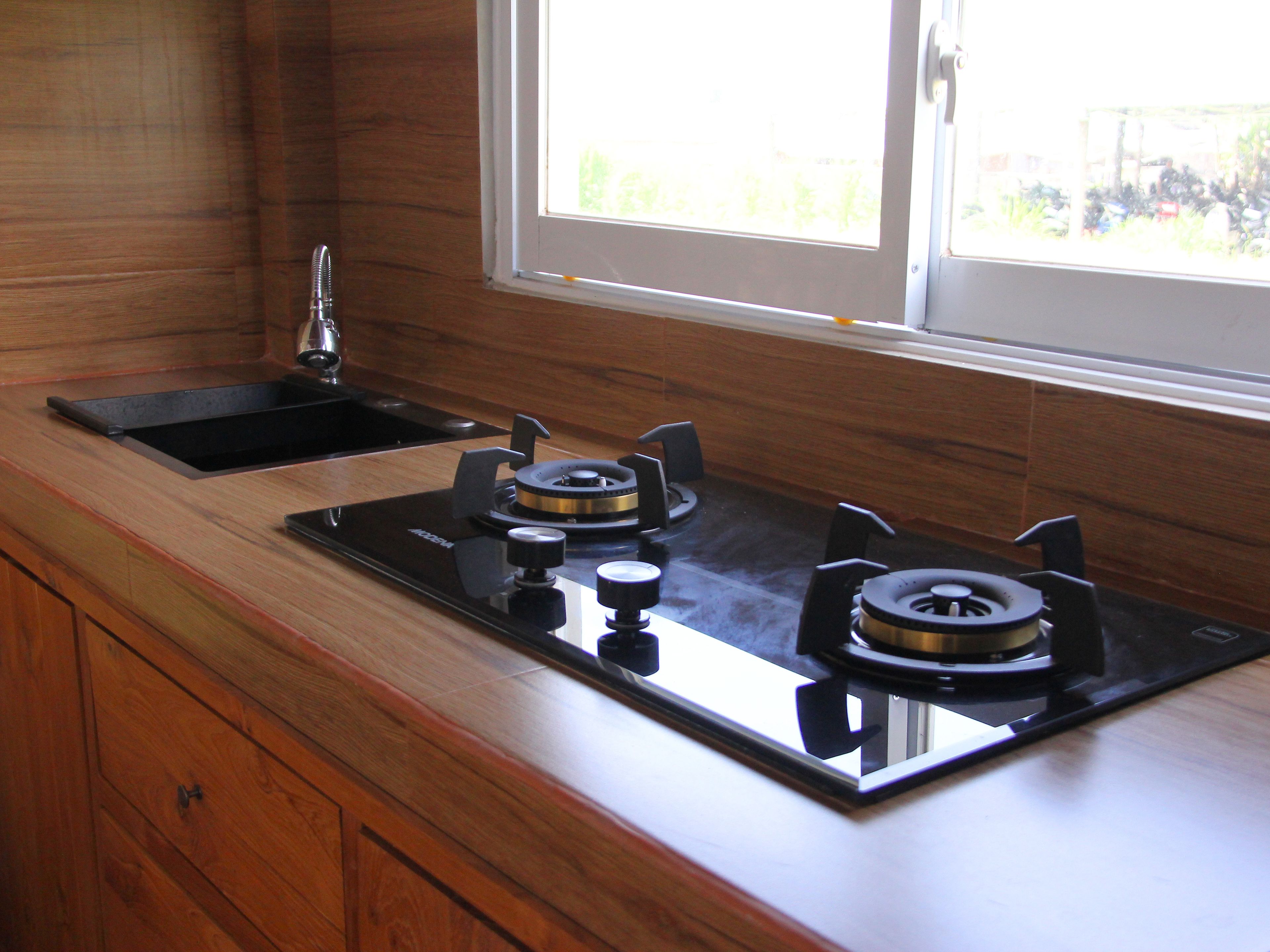 A kitchen with a black stovetop, wooden cabinets, and a window with a view of greenery.