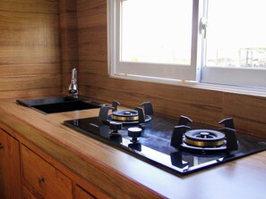A kitchen with a gas stove, a sink, and wooden cabinetry. - Gung Wah Guesthouse by AGATA (Ubud)