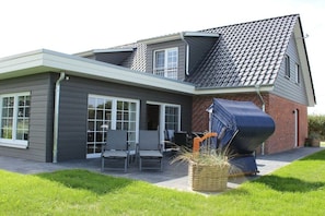 A modern house with a grey exterior, a sloped roof, and a patio area with outdoor furniture. - Holiday home in Pommerby with swimming pool (Pommerby)