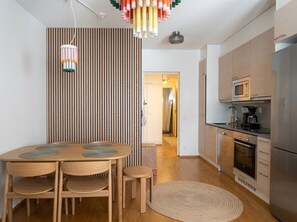 A modern kitchen with a dining area, featuring a round wooden table, chairs, and a striped partition. - Stylish 1BR Apt with Prime Location (Helsinki)