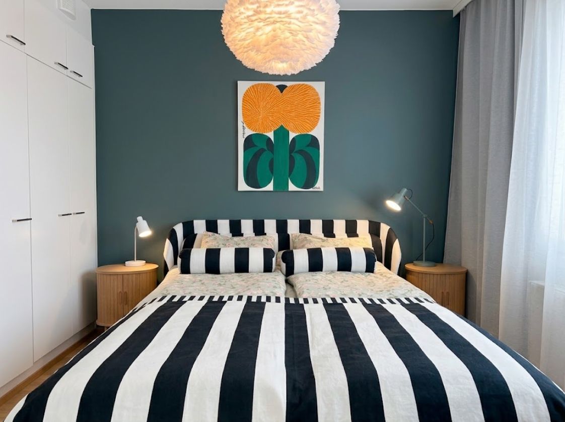 Un dormitorio con una cama, dos mesitas de noche, un aplique colgante y una obra de arte en la pared.