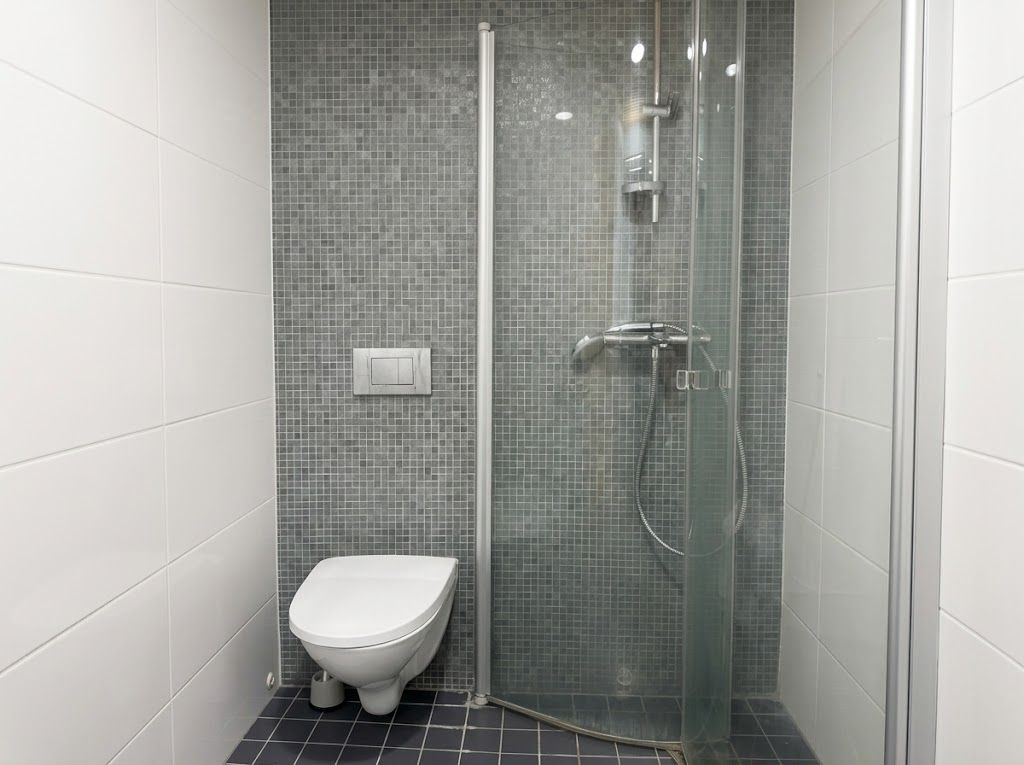 Un baño con ducha envuelta en vidrio, inodoro blanco y piso de baldosas.