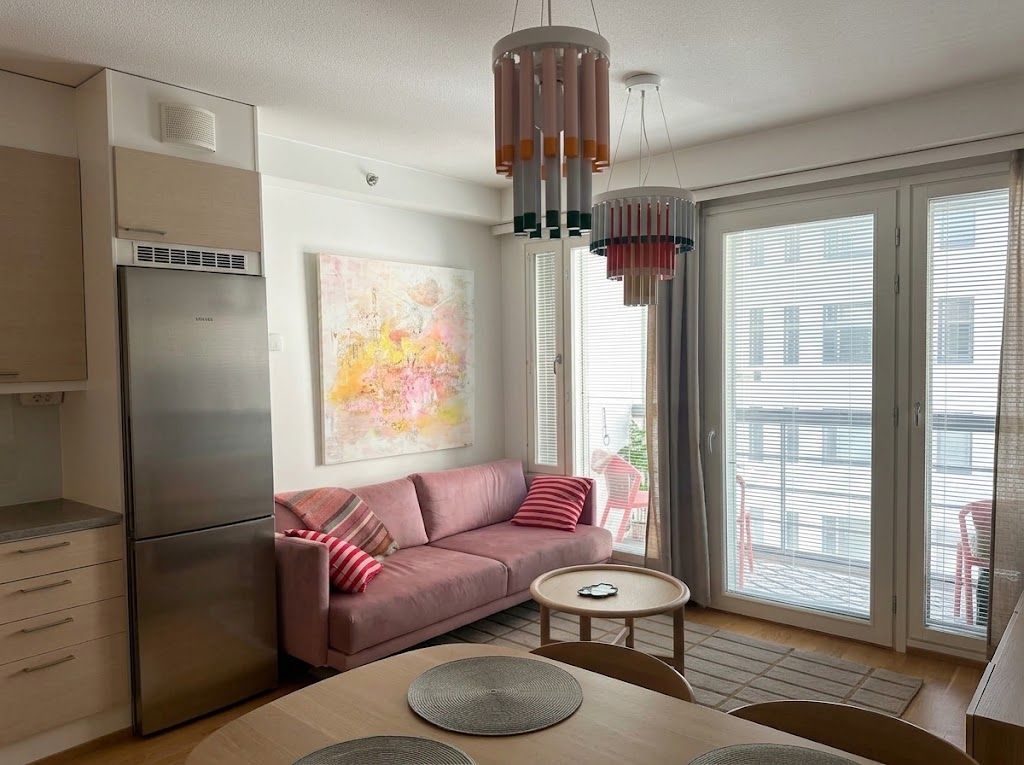 Una cocina moderna con un refrigerador de acero inoxidable, un sofá rosa y una zona de comedor con una mesa redonda.