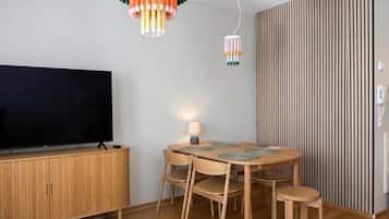 Un soggiorno moderno con una TV a schermo piatto, un tavolo da pranzo in legno con sedie e un lampadario decorativo.