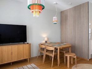 A modern living room with a flat-screen TV, wooden dining table with chairs, and a decorative hanging light fixture. - Stylish 1BR Apt with Prime Location (Helsinki)