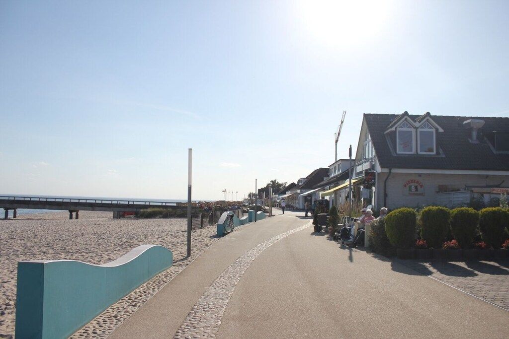 Une promenade en bord de mer avec un chemin pavé, une plage en arrière-plan et des bâtiments abritant des boutiques et des terrasses.