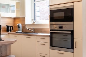 A modern kitchen with a built-in oven, a coffee machine, and a window with a view. - Holiday home with 2 bedrooms (Kellenhusen)