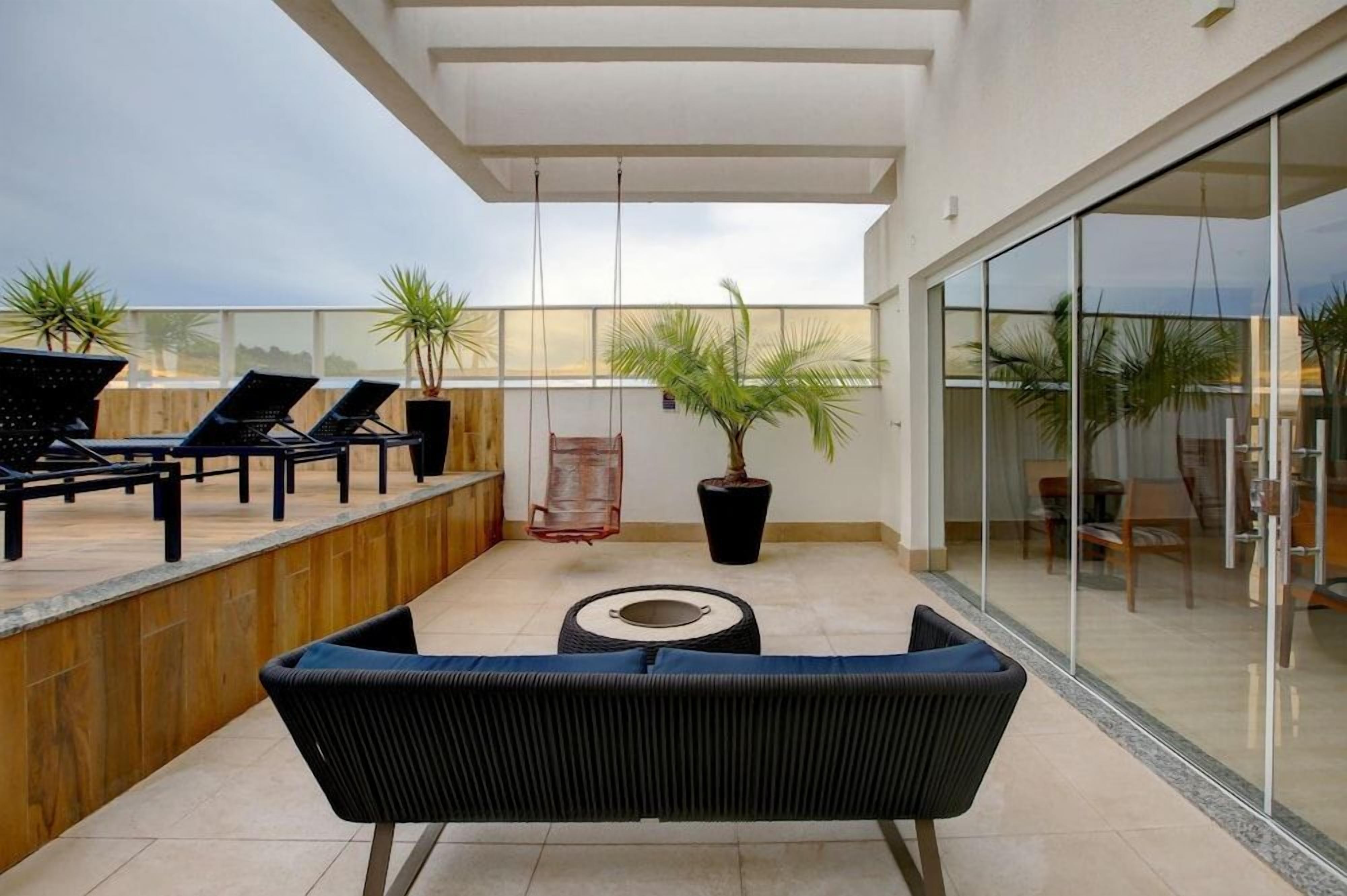Uma área de estar moderna ao ar livre, com cadeiras de lounge, um sofá, uma planta em vaso e uma cadeira balanço.