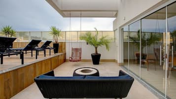 Uma área de estar moderna ao ar livre, com cadeiras de lounge, um sofá, uma planta em vaso e uma cadeira balanço.
