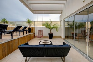 Uma área de estar moderna ao ar livre, com cadeiras de lounge, um sofá, uma planta em vaso e uma cadeira balanço.