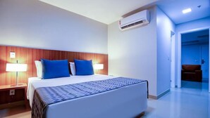Een hotelkamer met een bed, twee bedlampen, een houten hoofdeinde, een beddengoed met een patroon en een airconditioning.