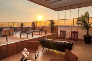Terraza en la azotea con mobiliario y plantas en macetas, con vistas a un atardecer.