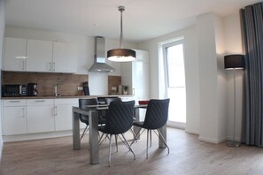 A modern kitchen with white cabinets, a dining table with black chairs, and a pendant light. - Sonnengarten 17 in Kellenhusen (Kellenhusen)