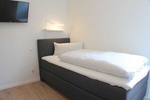 A single bed with a dark headboard, a bedside lamp, and a flat-screen TV mounted on the wall. - Sonnengarten 17 in Kellenhusen (Kellenhusen)