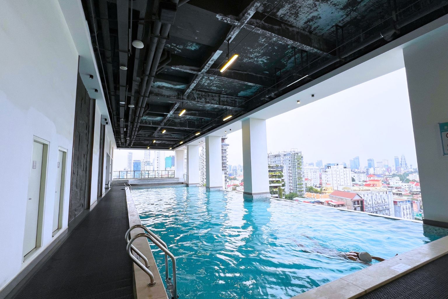 Une piscine à débordement intérieure offrant une vue sur la ville, un long couloir et un design de plafond moderne.
