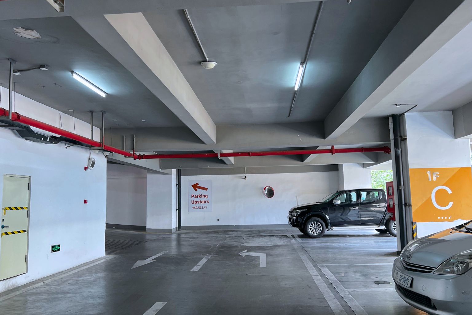 Un parking avec des flèches directionnelles peintes sur le sol, un panneau indiquant que le parking se trouve à l’étage, et un extincteur fixé au mur.