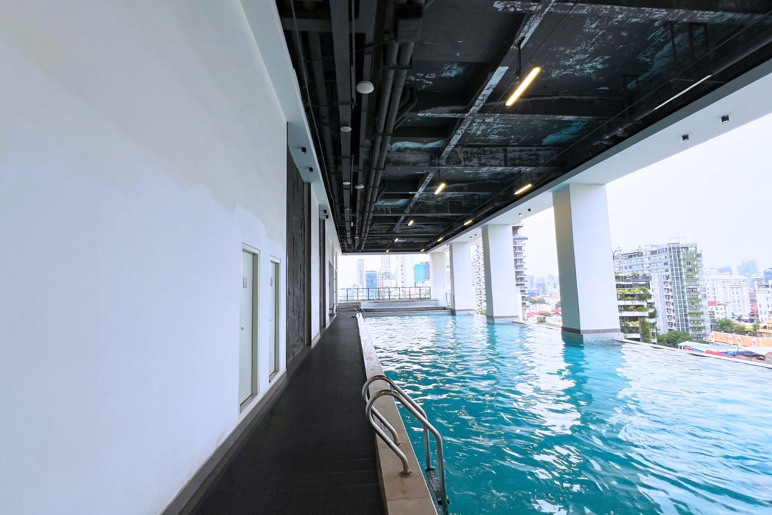 An indoor swimming pool with a view of a cityscape, featuring a modern architectural design with a high ceiling and visible structural elements.