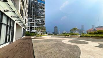 A rooftop terrace with a wooden deck, circular seating areas, and a view of a city skyline.