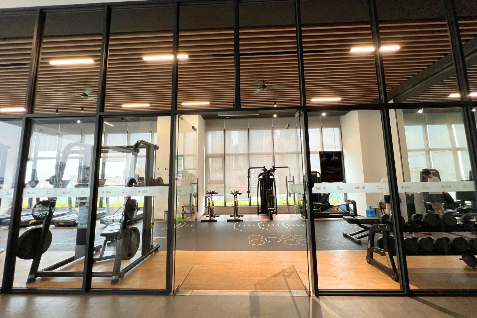 A gym with various exercise equipment, large windows, and a modern interior design.