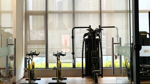 Une salle de sport équipée de matériel d’exercice et dotée de grandes fenêtres donnant sur un panorama urbain.